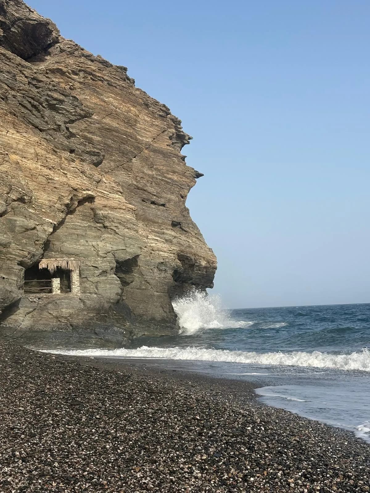 La caseta de piedra encajada en el acantilado de la Playa del Ruso, con una ola rompiendo