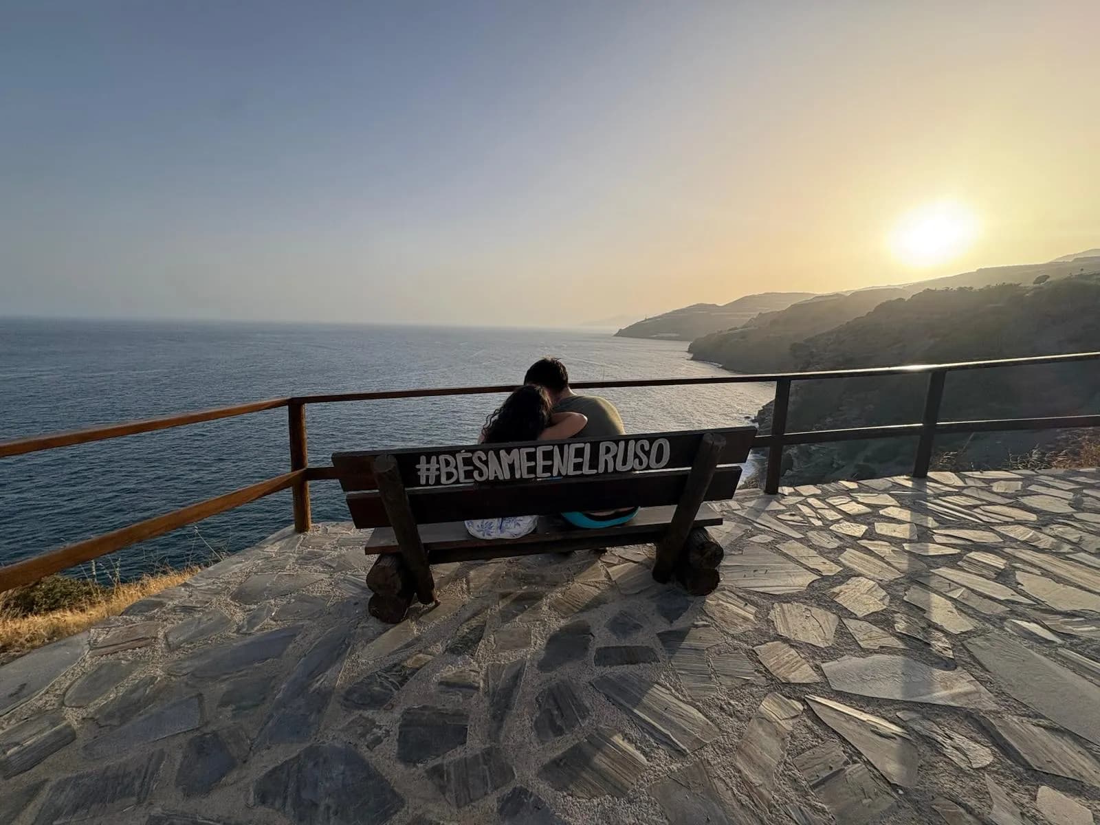 Una pareja en el banco del mirador “Bésame en el Ruso”, frente a la cala al atardecer