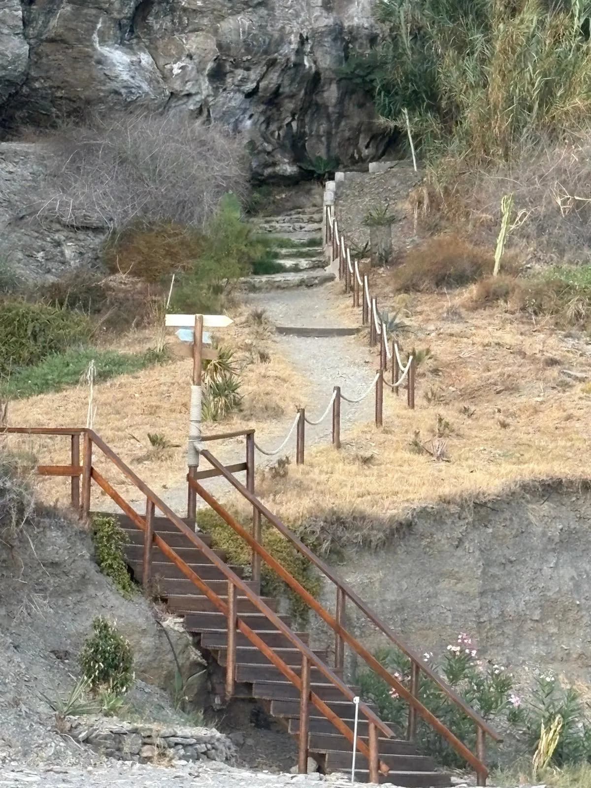 El sendero de madera que baja a la Playa del Ruso, con escaleras y barandas entre la roca